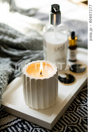 Burning white handmade candle and cosmetic bottles on minimalist tray 80807277