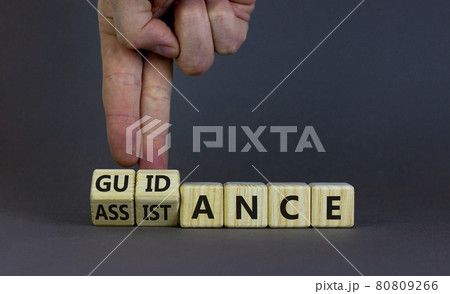 Guidance and assistance symbol. Businessman turns cubes, changes words 'assistance' to 'guidance'. Beautiful grey background, copy space. Business, guidance and assistance concept. Guidance and assistance symbol. Businessman turns cubes, changes words 'assistance' to 'guidance'. Beautiful grey background, copy space. Business, guidance and assistance concept. 80809266