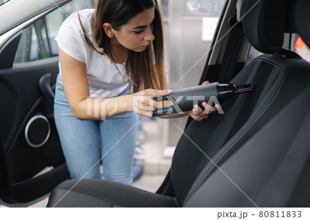Female using portable vacuum cleaner in her car. Electrical vacuum in woman's hand clean car inside from dust. Self servise car wash Female using portable vacuum cleaner in her car. Electrical vacuum in woman's hand clean car inside from dust. Self servise car wash 80811833
