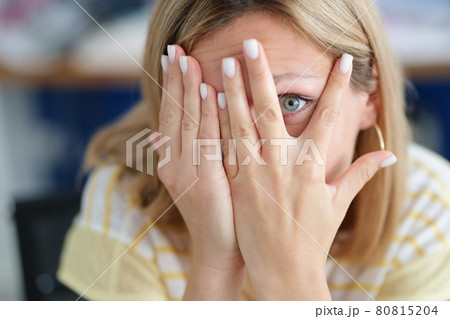 Woman covers face with her hand looking through fingers closeup Woman covers face with her hand looking through fingers closeup 80815204