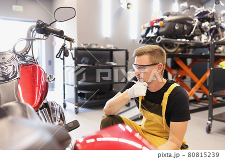 Pensive locksmith inspects technical condition of motorcycle in workshop Pensive locksmith inspects technical condition of motorcycle in workshop 80815239