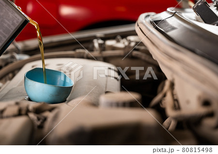 Auto mechanic pours oil into a car engine. 80815498