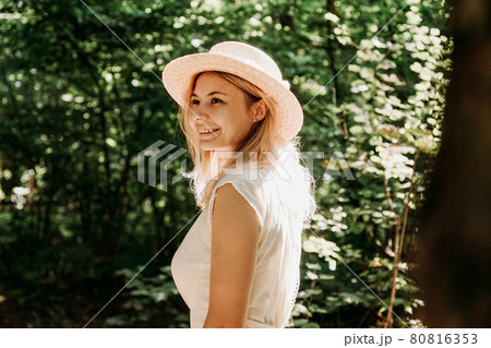 Beautiful young woman in a straw hat and white dress in a green park 80816353