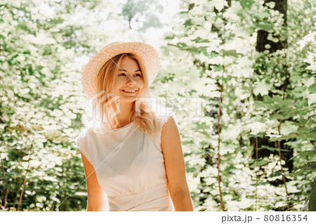 Beautiful young woman in a straw hat and white dress in a green park 80816354