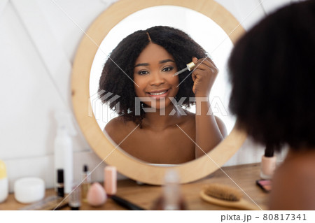 Beauty routines for healthy skin. Black woman applying hydrating serum or hyalurinic acid near mirror at home Beauty routines for healthy skin. Black woman applying hydrating serum or hyalurinic acid near mirror at home 80817341