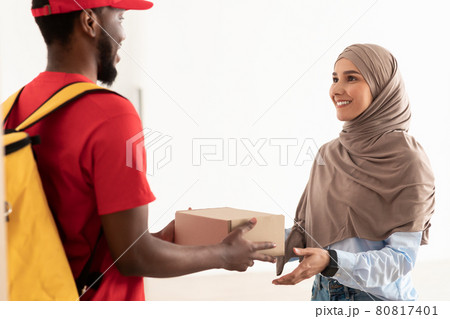 Black delivery man holding box giving it to muslim woman 80817401