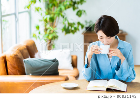 リビングでコーヒーを飲みながら読書をするミドルの女性 80821145