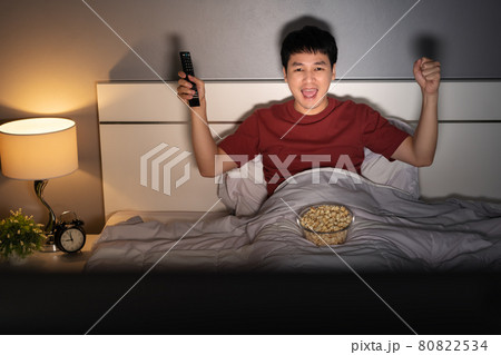 cheerful man watching sport TV with arm raised on a bed at night cheerful man watching sport TV with arm raised on a bed at night 80822534