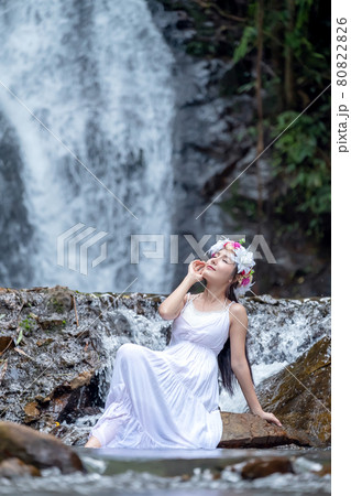 A beautiful young lady relaxes in nature near a waterfall. 80822826