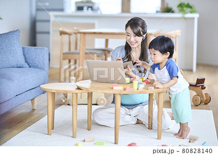 子供のいるリビングでオンライン会議をする女性の写真素材 子供のいるリビングでオンライン会議をする女性の写真素材