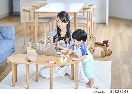 子供のいるリビングでオンライン会議をする女性の写真素材 子供のいるリビングでオンライン会議をする女性の写真素材
