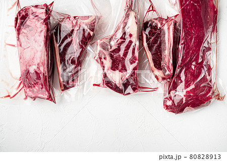 Vacuum packed organic raw beef classic cuts, tomahawk, t bone, club steak, rib eye and tenderloin cuts, on white stone background, top view flat lay, with copy space for text 80828913