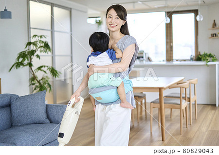 1歳半の息子を抱っこしながら掃除をする母親 80829043