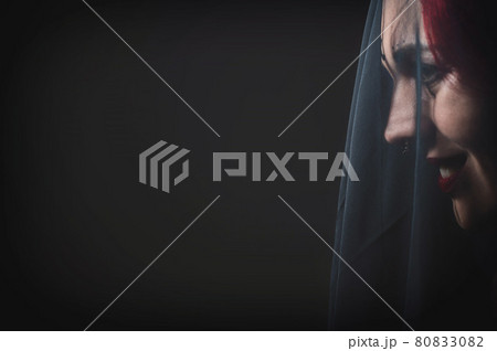 Profile of a woman in a black veil. Costume Dead bride for Halloween. Portrait of an evil grinning Witch in front of a coven. 80833082