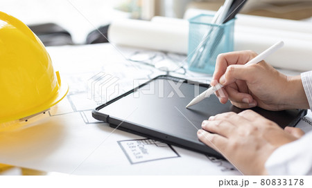Young man using tablet plotting a system of building structures in blueprints, Architects or engineers are designing buildings using tablet to calculate the physical structure to be correct. Young man using tablet plotting a system of building structures in blueprints, Architects or engineers are designing buildings using tablet to calculate the physical structure to be correct. 80833178