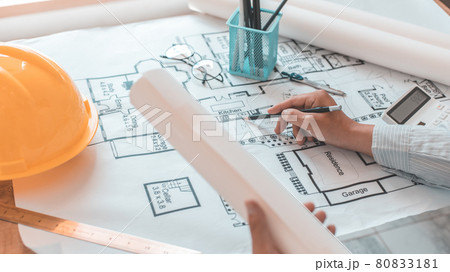 Architectural building design and construction plans with blueprints, Young man was designing a building or architecture with a pen ruler, pencil, tape measure, architect hat and other equipment. Architectural building design and construction plans with blueprints, Young man was designing a building or architecture with a pen ruler, pencil, tape measure, architect hat and other equipment. 80833181