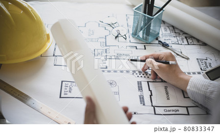 Architectural building design and construction plans with blueprints, Young man was designing a building or architecture with a pen ruler, pencil, tape measure, architect hat and other equipment. Architectural building design and construction plans with blueprints, Young man was designing a building or architecture with a pen ruler, pencil, tape measure, architect hat and other equipment. 80833347