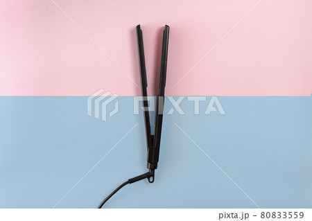 Electric curling iron with ceramic plates on blue and pink background. Top view. 80833559