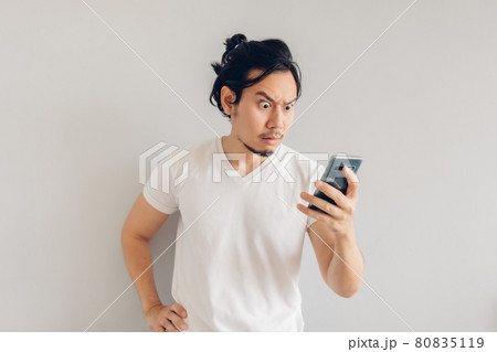 Serious long hair man in white casual t-shirt is using smartphone. Serious long hair man in white casual t-shirt is using smartphone. 80835119