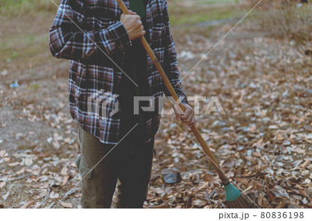 Gardening concept a male gardener using a coconut-leaf broom gathering the dry fallen leaves for cleaning the area Gardening concept a male gardener using a coconut-leaf broom gathering the dry fallen leaves for cleaning the area 80836198
