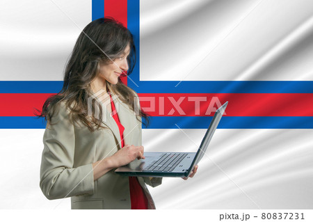 Freelance in Faroe Islands. Beautiful young woman freelancer uses laptop computer against the background of the flag of Faroe Islands 80837231