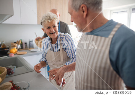Senior couple with friends having party indoors, talking when cooking. 80839019