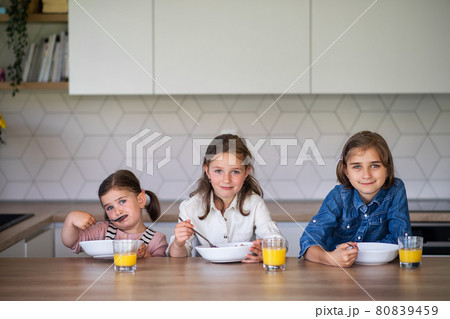Portrait of three girls sisters indoors at home, looking at camera when eating breakfast. Portrait of three girls sisters indoors at home, looking at camera when eating breakfast. 80839459