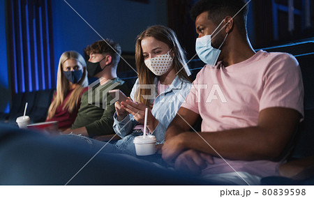 Cheerful young couple with smartphone in the cinema, coronavirus concept. Cheerful young couple with smartphone in the cinema, coronavirus concept. 80839598