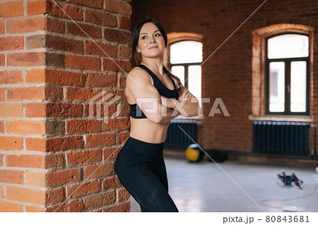 Portrait of happy muscular young athletic woman with strong beautiful body in black sportswear standing with arms crossed by brick wall. Portrait of happy muscular young athletic woman with strong beautiful body in black sportswear standing with arms crossed by brick wall. 80843681