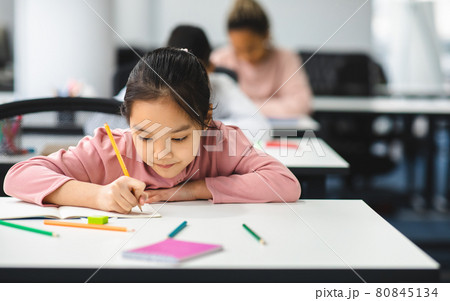 Portrait of small asian girl sitting at desk and writing Portrait of small asian girl sitting at desk and writing 80845134