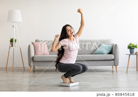 Overjoyed Indian woman sitting on scales, gesturing YES, excited over result of her weight loss diet at home Overjoyed Indian woman sitting on scales, gesturing YES, excited over result of her weight loss diet at home 80845618