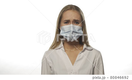 A nurse wearing a medical mask reveals that she has symptoms of powdery looking at the camera in a medical gown and purple disposable gloves. Isolated on white background. 4k resolution footage 80846692