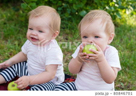 Twin girls looking up with an appetite eat apples in the fresh air 80846701