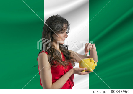 Economy in Nigeria. Accumulating and saving money in Nigeria. Woman putting money coin in piggy bank for saving money and plan finance Economy in Nigeria. Accumulating and saving money in Nigeria. Woman putting money coin in piggy bank for saving money and plan finance 80848960