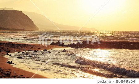 Empty wild beach lit by golden sunset. Small waves over rock, hills in hazy background. Empty wild beach lit by golden sunset. Small waves over rock, hills in hazy background. 80849554