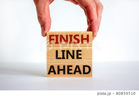 Finish line ahead symbol. Male hand builds stack from blocks with words 'Finish line ahead'. White table. Beautiful white background. Copy space. Business and finish line ahead concept. Finish line ahead symbol. Male hand builds stack from blocks with words 'Finish line ahead'. White table. Beautiful white background. Copy space. Business and finish line ahead concept. 80850510