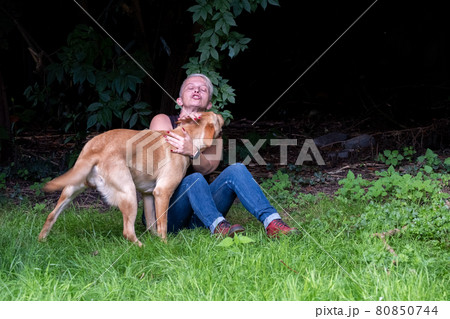 Handsome woman Plays with her Happy Golden labrador Retriever Dog on the Backyard Lawn. Woman Has 80850744