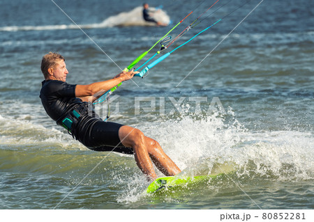 Young adult caucasian fit male person enjoy riding kite surf board in sun uv protection suit on bright sunny day against blue sky at sea or ocean shore. Watersport adrenaline fun adventure acitivity 80852281