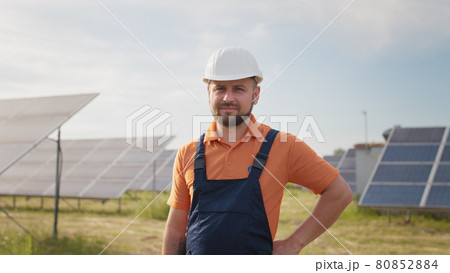 Portrait of happy male engineer in protective helmet looking to camera. Handsome man in uniform smiling while standing at solar power farm. Concept of green energy. Industrial people. Energy Portrait of happy male engineer in protective helmet looking to camera. Handsome man in uniform smiling while standing at solar power farm. Concept of green energy. Industrial people. Energy 80852884