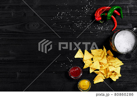 Snack for party, chips, nachos with sauces: tomato ketchup , mustard and mug of beer on a black background. Top view, copy space Snack for party, chips, nachos with sauces: tomato ketchup , mustard and mug of beer on a black background. Top view, copy space 80860286