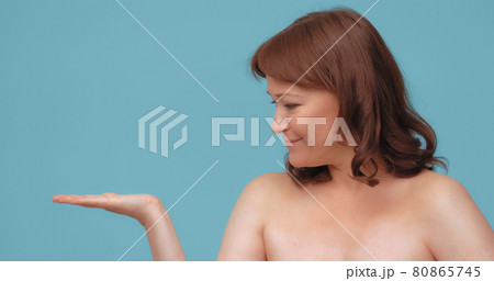 Cheerful mature woman holding open hand for embedding skin care visualization. Smiling woman advertise anti-age cream isolated on color background Cheerful mature woman holding open hand for embedding skin care visualization. Smiling woman advertise anti-age cream isolated on color background 80865745