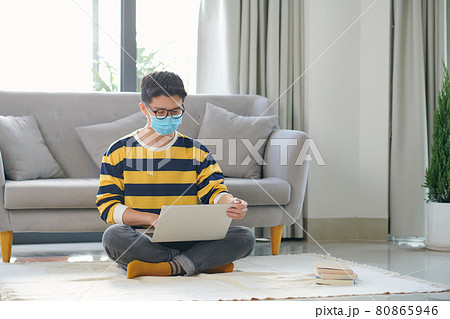 Asian man is sitting on the floor with a book and laptop Asian man is sitting on the floor with a book and laptop 80865946