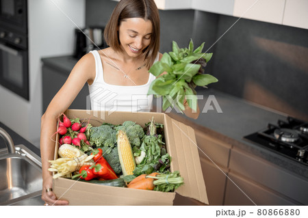 Woman with fresh vegetables packed in cardboard box at kitchen 80866880