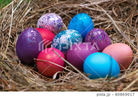Multicolored purple and blue eggs with glitters composed in heap on straw nest for Easter holiday 80869017