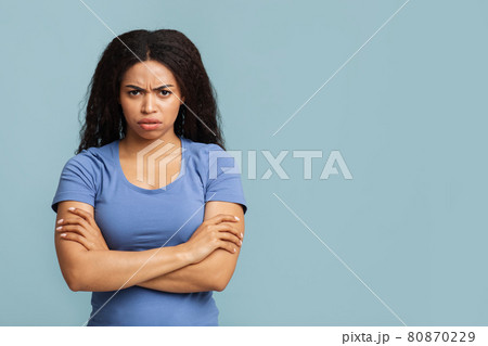 Grumpy woman. Portrait of serious black lady standing with crossed arms, posing over blue background with free space Grumpy woman. Portrait of serious black lady standing with crossed arms, posing over blue background with free space 80870229