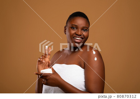 Beautiful young african american woman applying body moisturizer 80870312