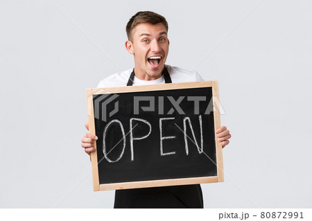 Small retail business owners, cafe and restaurant employees concept. Cheerful smiling barista greeting guests, salesman showing we are open sign and grinning upbeat, white background 80872991