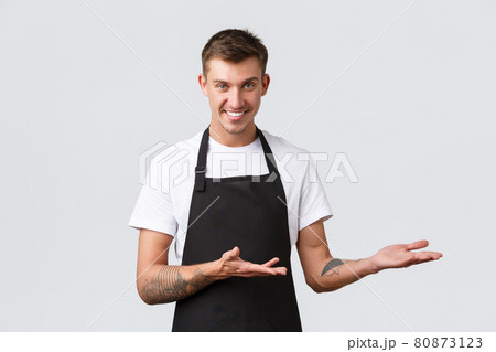 Cafe and restaurants, coffee shop owners and retail concept. Handsome salesman, waiter in black apron pointing right, inviting come inside, showing way or introducing discounts, white background Cafe and restaurants, coffee shop owners and retail concept. Handsome salesman, waiter in black apron pointing right, inviting come inside, showing way or introducing discounts, white background 80873123
