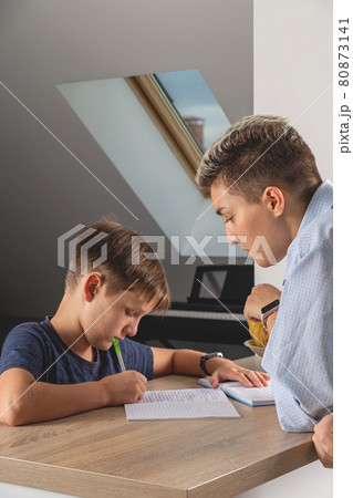 Kid boy doing homework at kitchen table with book 80873141