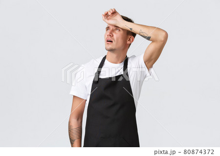Employees, grocery stores and coffee shop concept. Tired waiter looking up and exhaling from fatigue, barista wipe sweat from forehead need break, feeling exhausted serving tables, white background 80874372